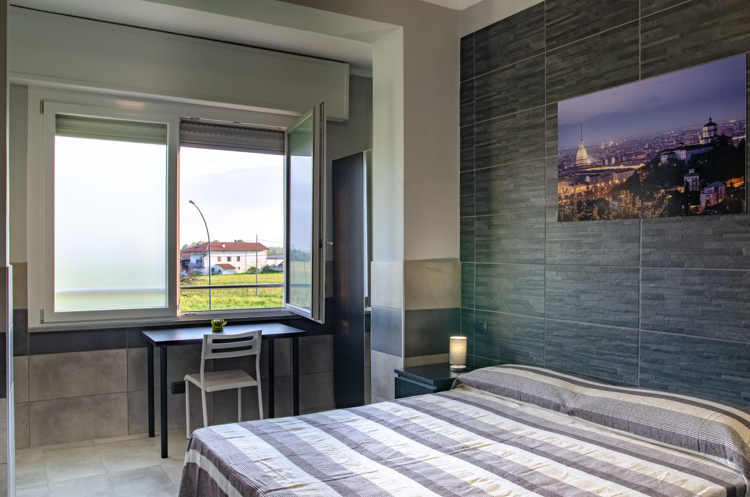 A bedroom with a large window, a desk, and a bed.