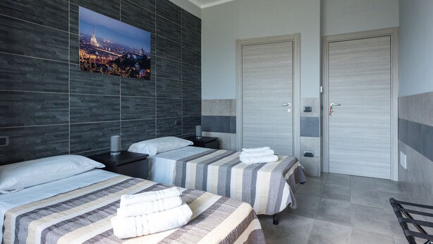A hotel room with two beds, a large cityscape picture on the wall, and a closed door. - La Montrucca camere (Caselle Torinese)
