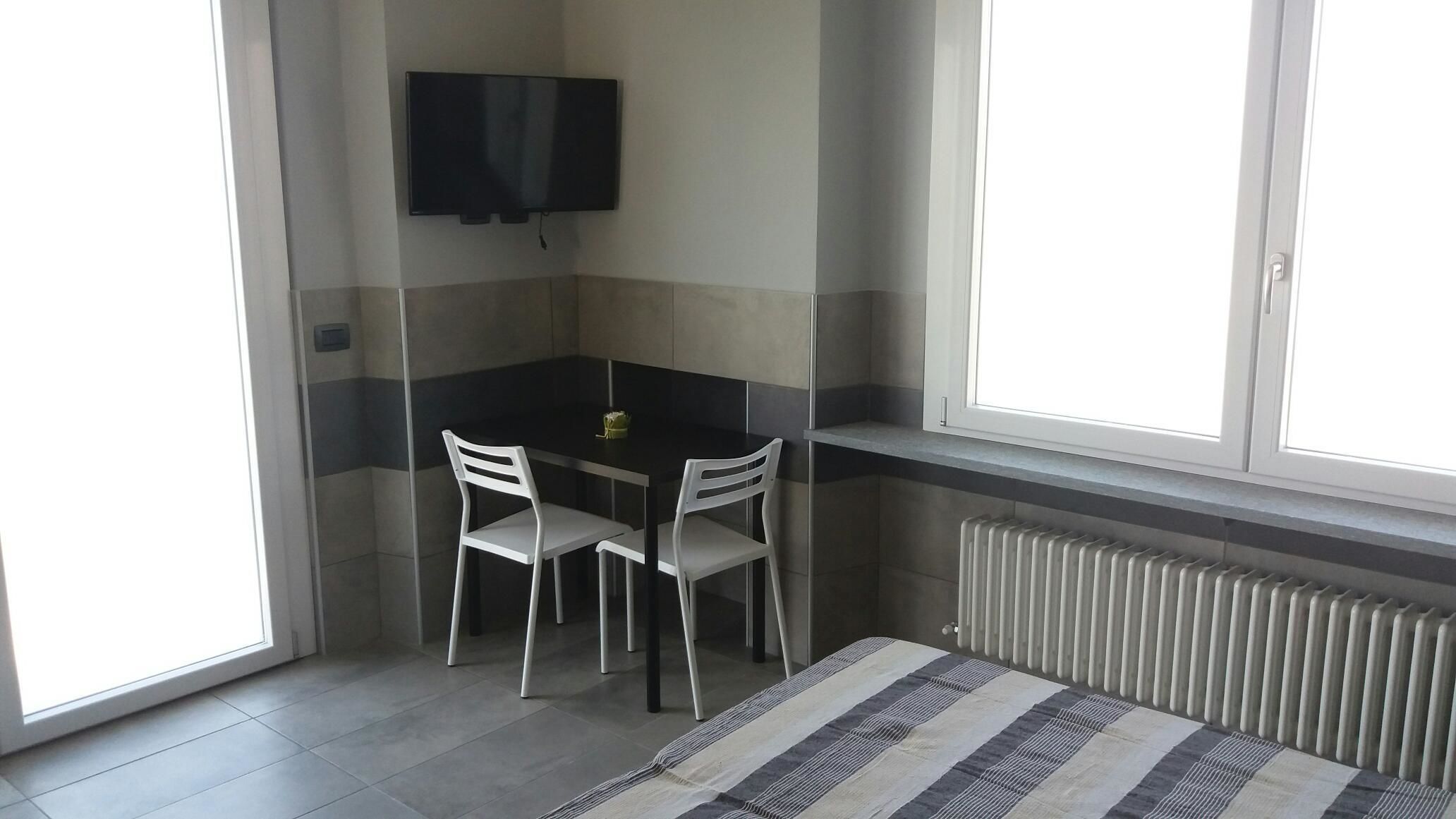 A small, modern room with a black table and two white chairs, a flat-screen TV mounted on the wall, and a window with a view of the outside.