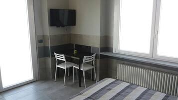 A small, modern room with a black table and two white chairs, a flat-screen TV mounted on the wall, and a window with a view of the outside.