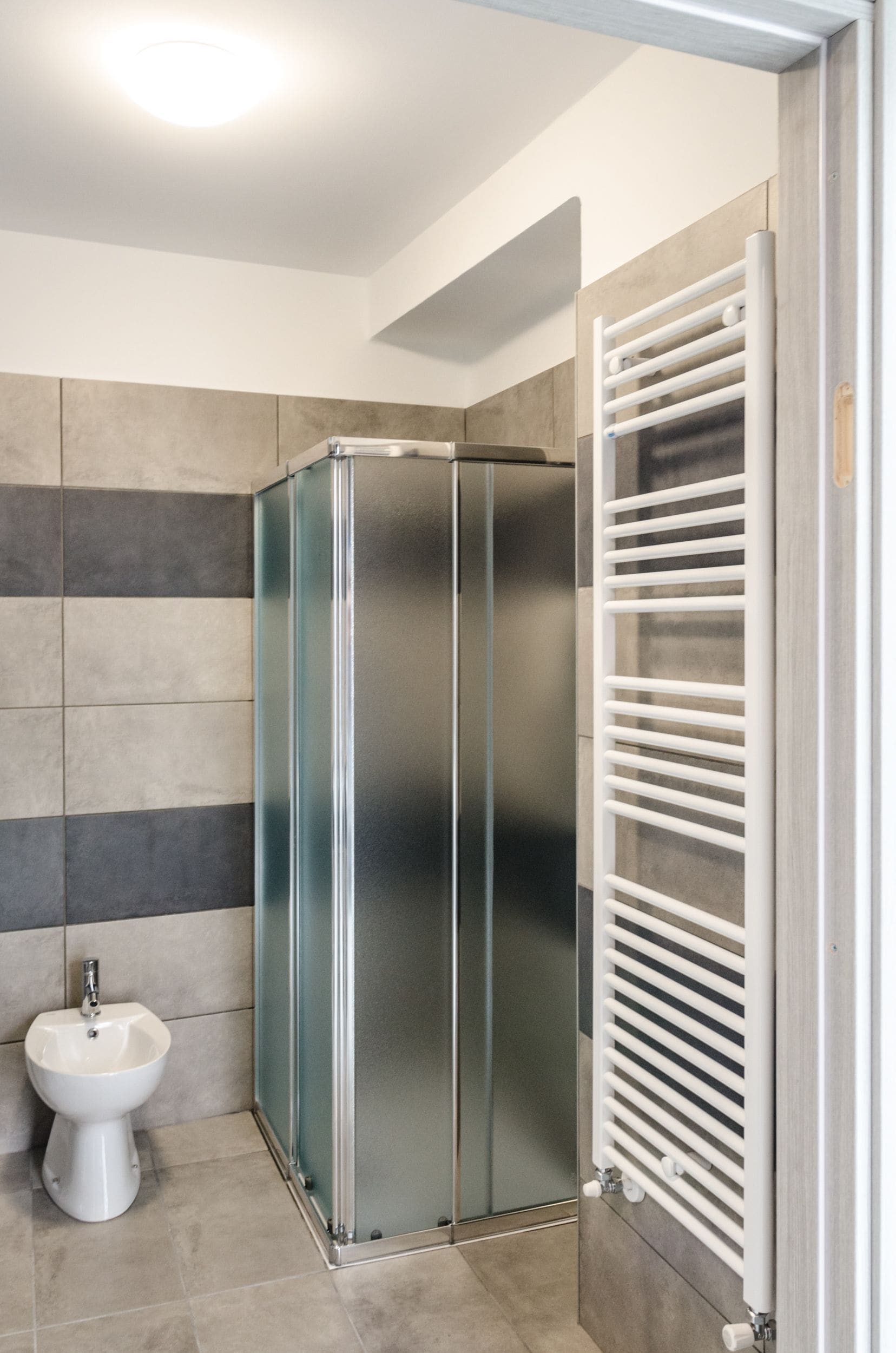 Une salle de bain moderne avec une douche à parois de verre, un lavabo sur colonne blanc et un porte-serviettes blanc.