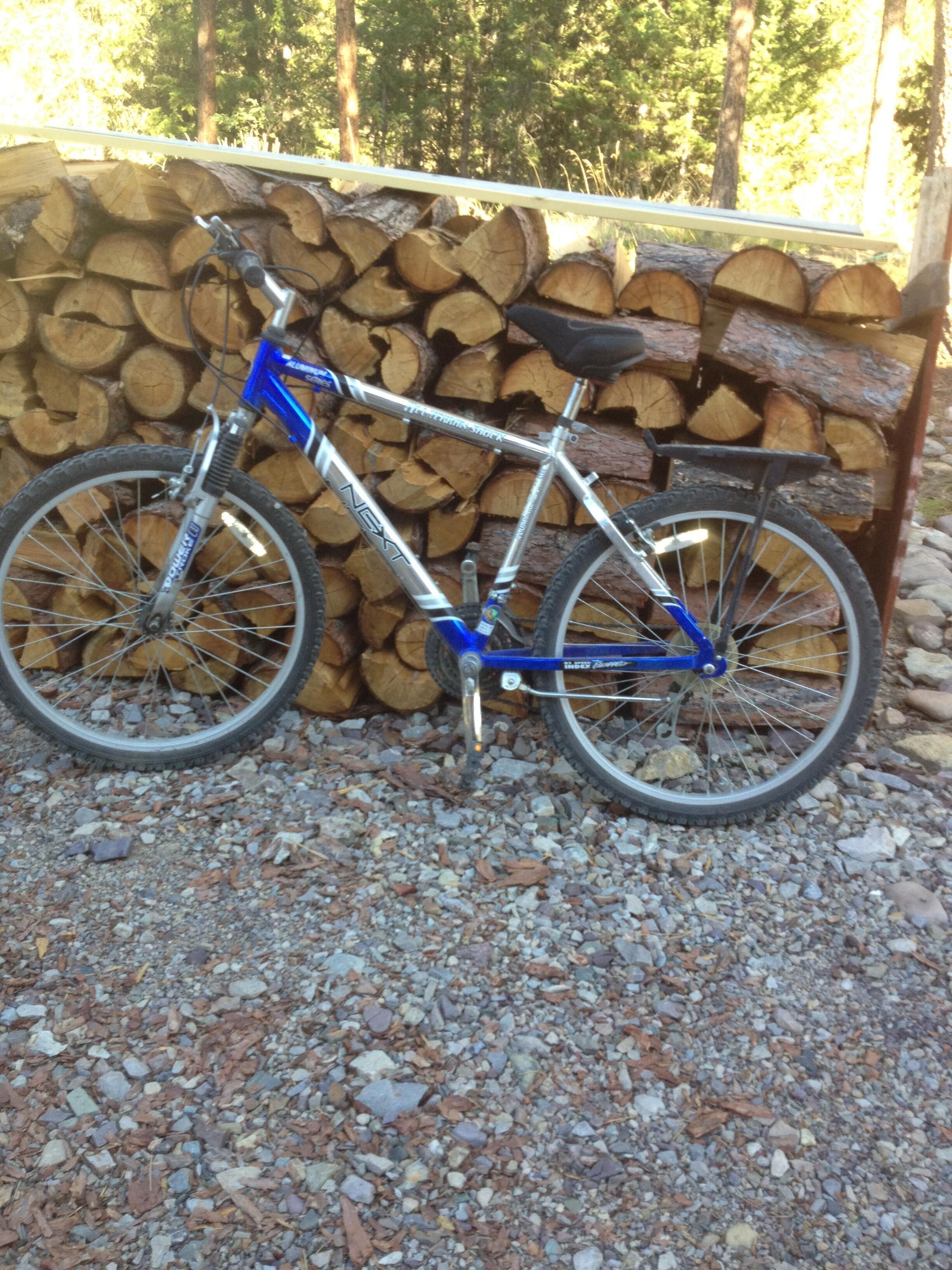 A bicycle parked on gravel with a pile of logs in the background.