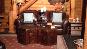 Een knus houten blokhutinterieur met een leren bank, twee fauteuils, een bijzettafeltje en een lamp.