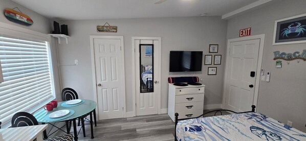 Una habitación con una mesa de comedor, sillas, una cama, un televisor y dos puertas.