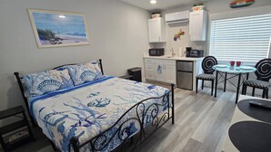 Een compacte kamer met een bed, kitchenette, eethoek en een deur naar een balkon.