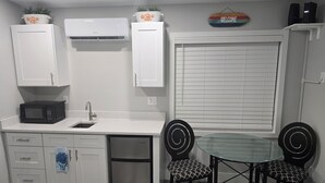 Een kleine keuken met witte kastjes, een magnetron, een spoelbak en een glazen tafel met twee stoelen.