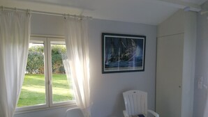A room with a window, a painting, a chair, and a table.