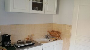 A kitchen with white cabinets, a sink, a coffee maker, and a trash bin.