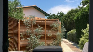 An outdoor patio area with a table and two chairs, a wooden fence, and a pathway leading to a building.
