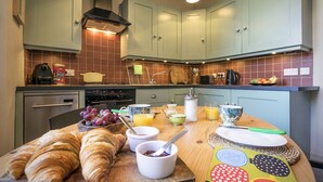 A kitchen with teal cabinets, a wooden countertop, and various breakfast items including croissants, bowls of jam, and a fruit bowl. - Stylish City Centre Apartment (Edinburgh)