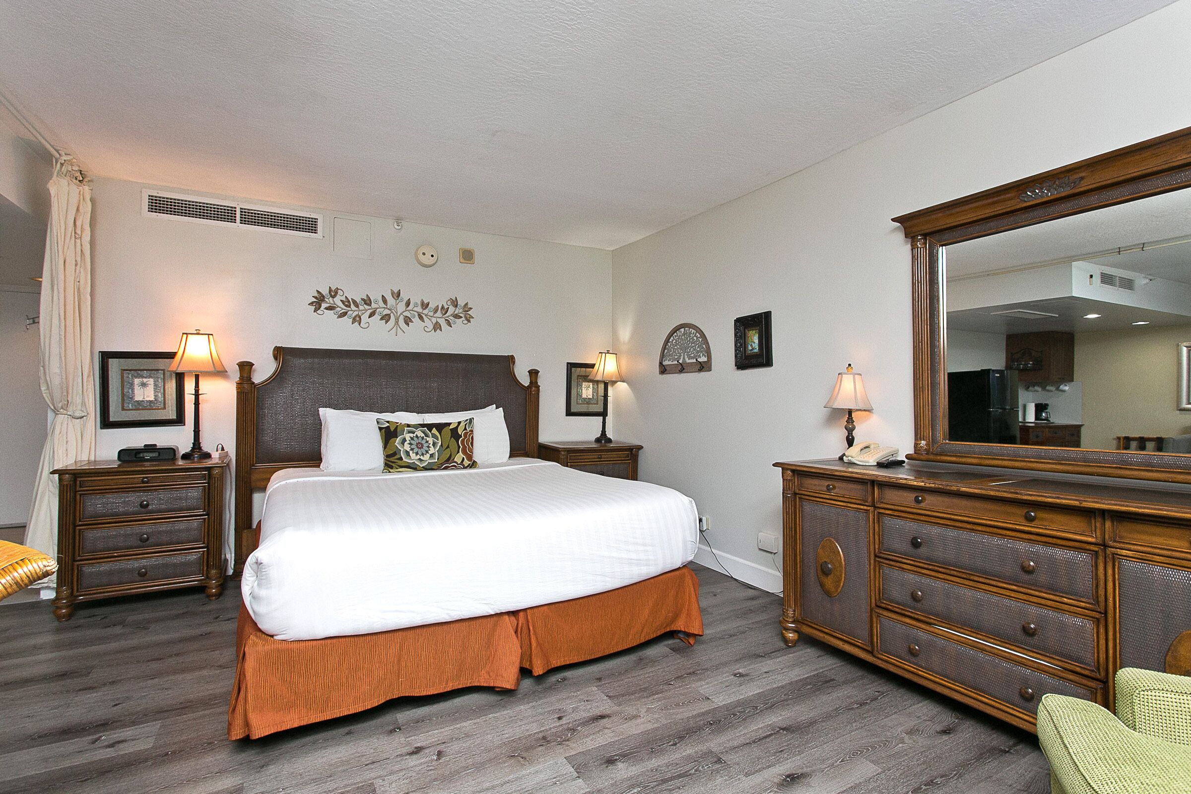 A hotel room with a large bed, two bedside tables with lamps, a dresser, and a mirror.