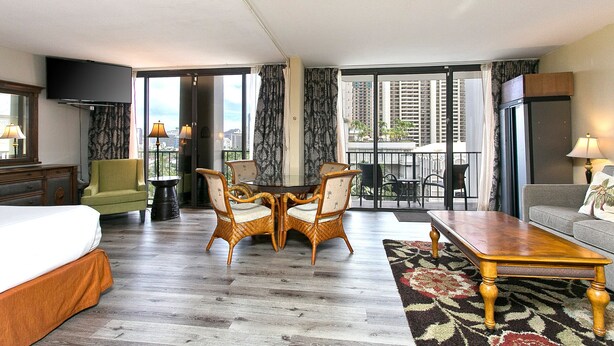 A hotel room with a bed, a dining table with chairs, a sofa, a TV, and a balcony with a view of the city. - Pool & close to Beaches, Elegant King Bed Studio (Sleeps 4) FREE Parking! (Honolulu)