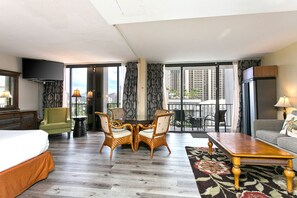 Een hotelkamer met een bed, een eettafel met stoelen, een bank, een televisie en een balkon met uitzicht over de stad.