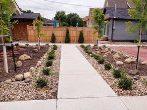 Stroll along the garden pathway, flanked by shrubs and rocks, to a rustic wooden fence.