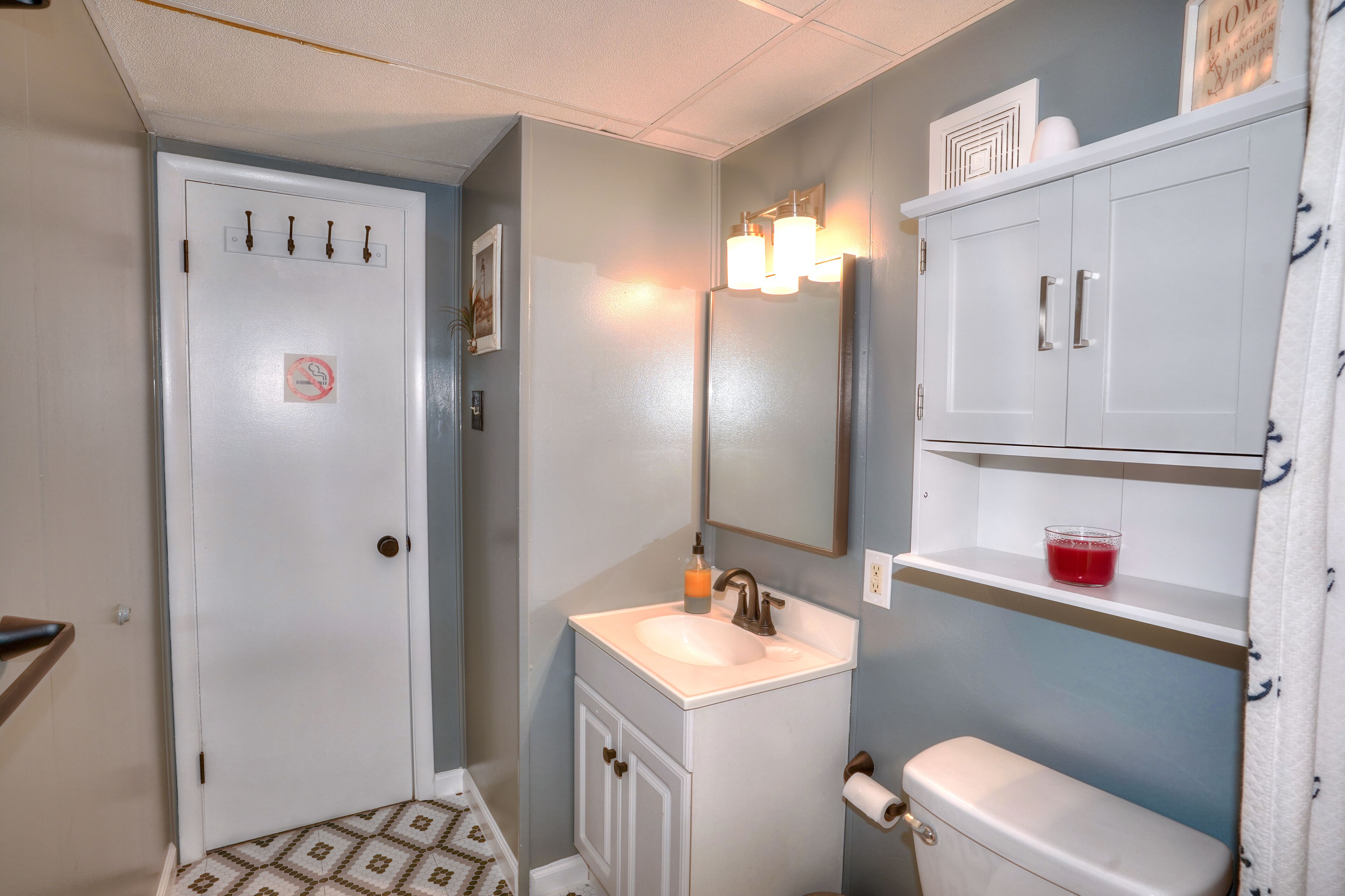 A bathroom with a white sink, a toilet, a mirror, and a cabinet with a red object on top.