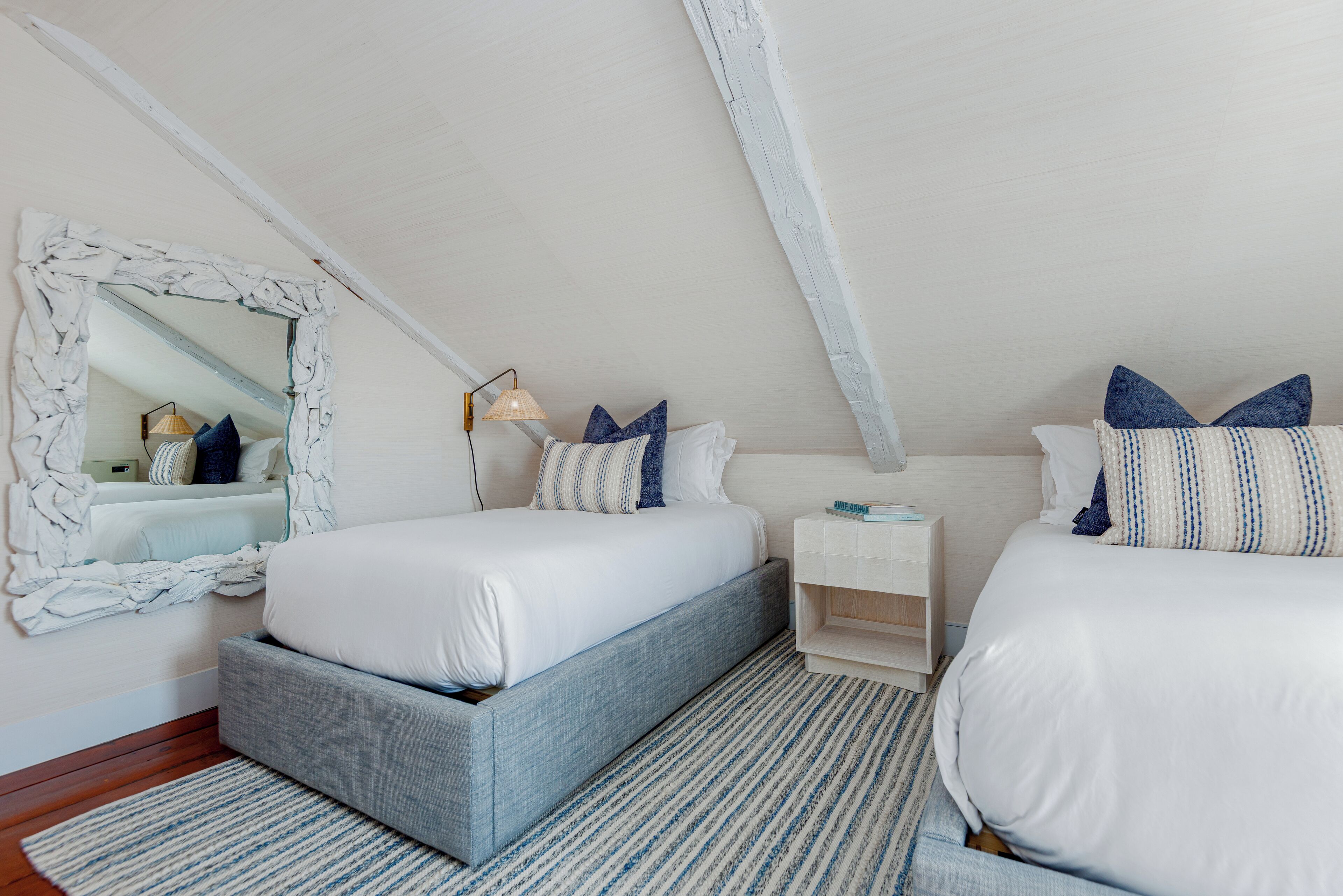 Une chambre avec deux lits, un grand miroir, des tables de chevet et un tapis à motifs.
