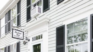 A white building with black shutters, a sign for Anchor Inn, and a small porch with steps. - Anchor Inn (Nantucket)