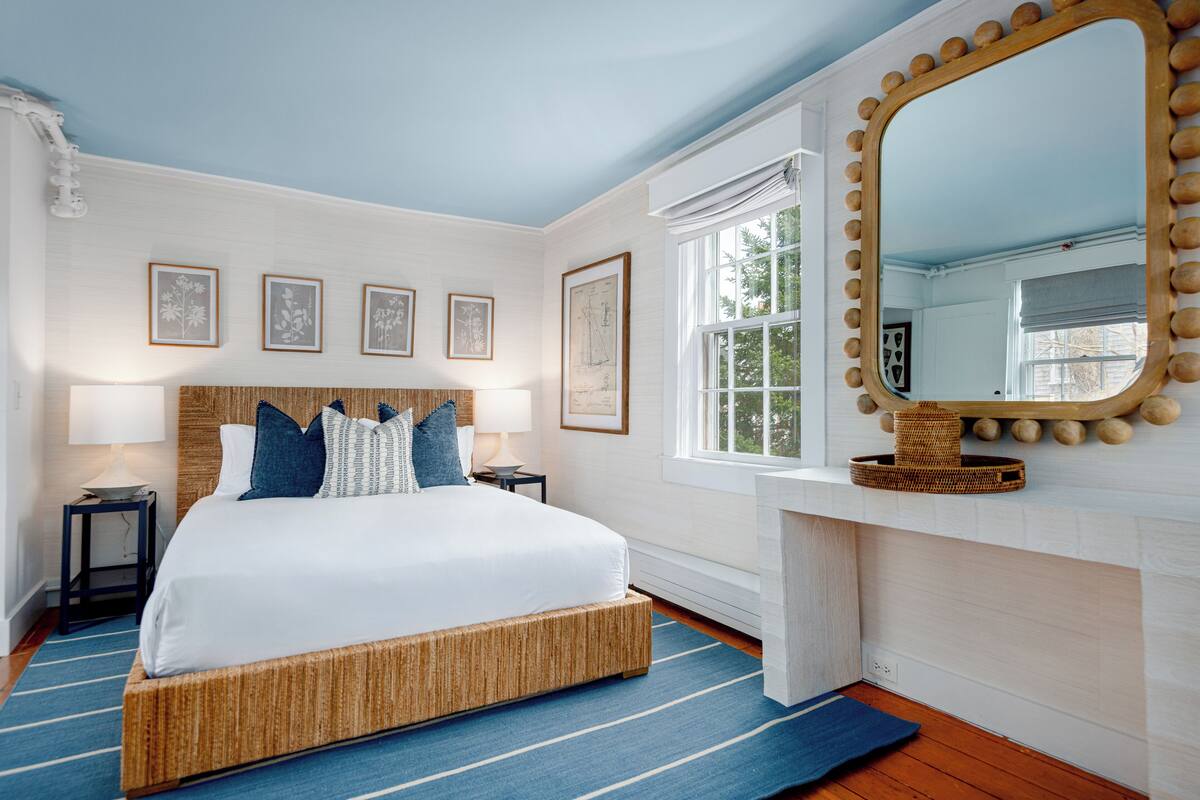 Quarto com uma cama grande, um espelho com moldura decorativa e obras de arte emolduradas na parede.