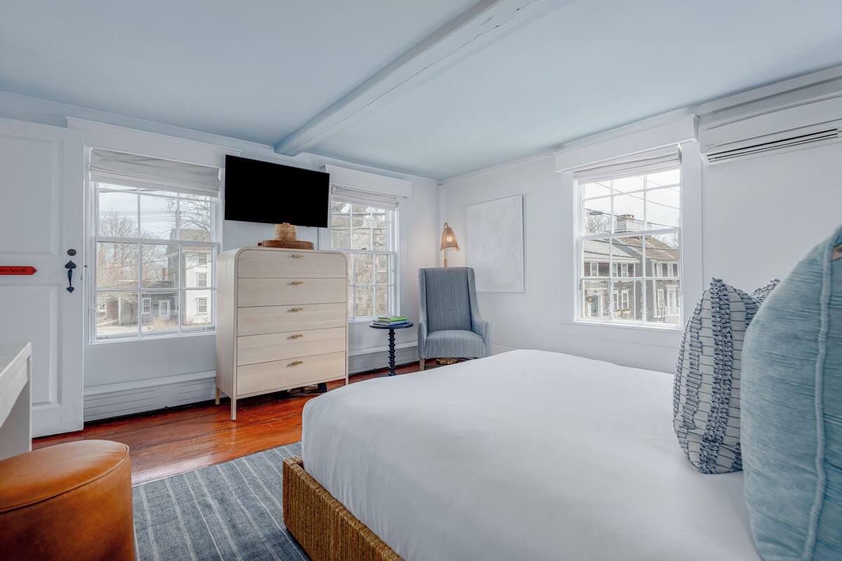 Quarto com uma cama grande, cômoda, cadeira e televisão na parede.