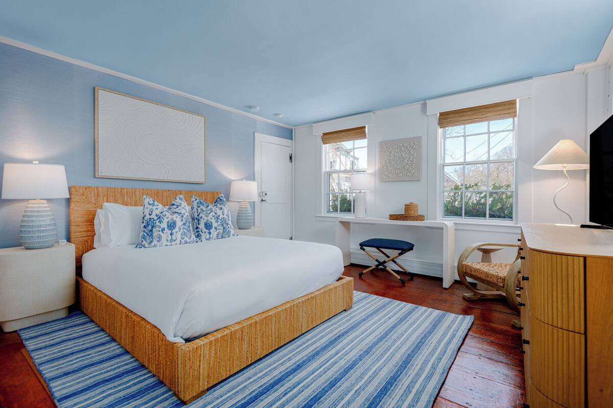 Quarto com uma cama grande, escrivaninha, cadeira e televisão.