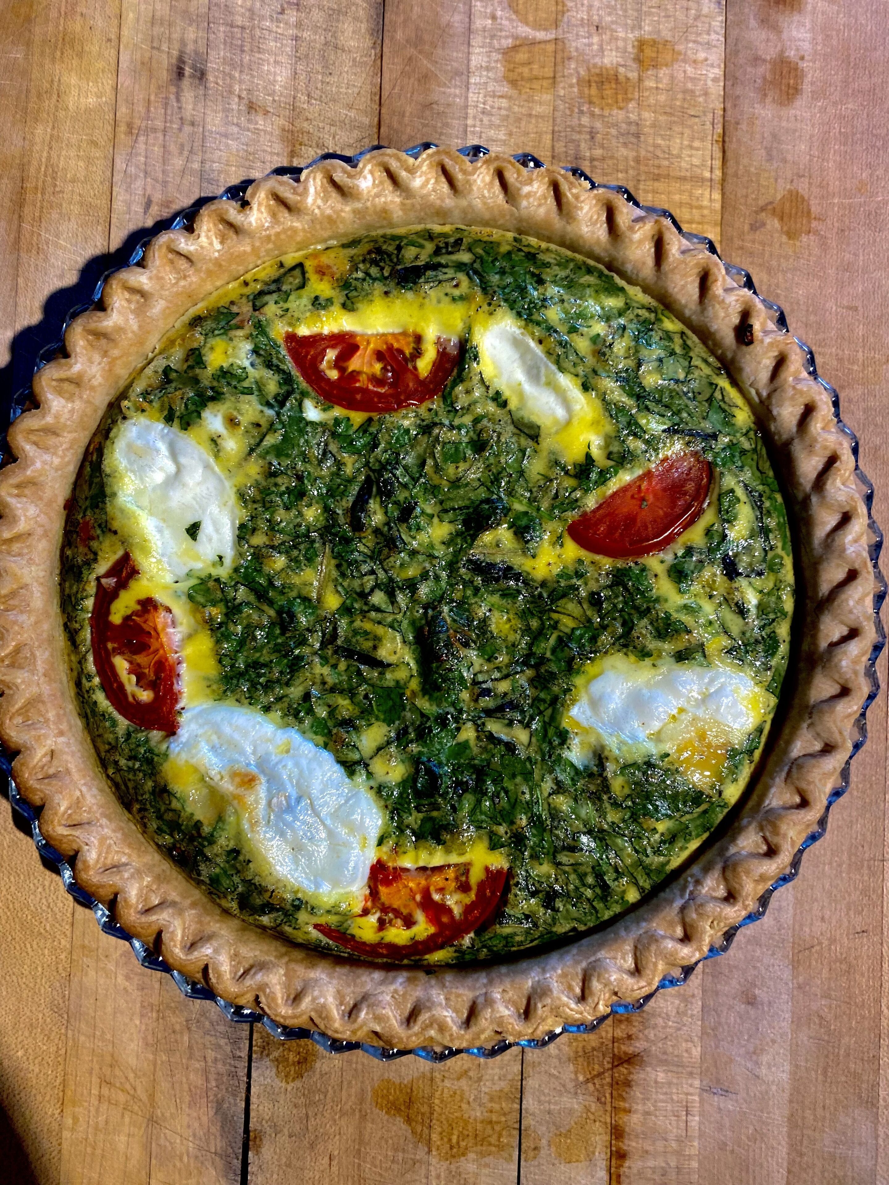 A quiche in a pie dish on a wooden surface.