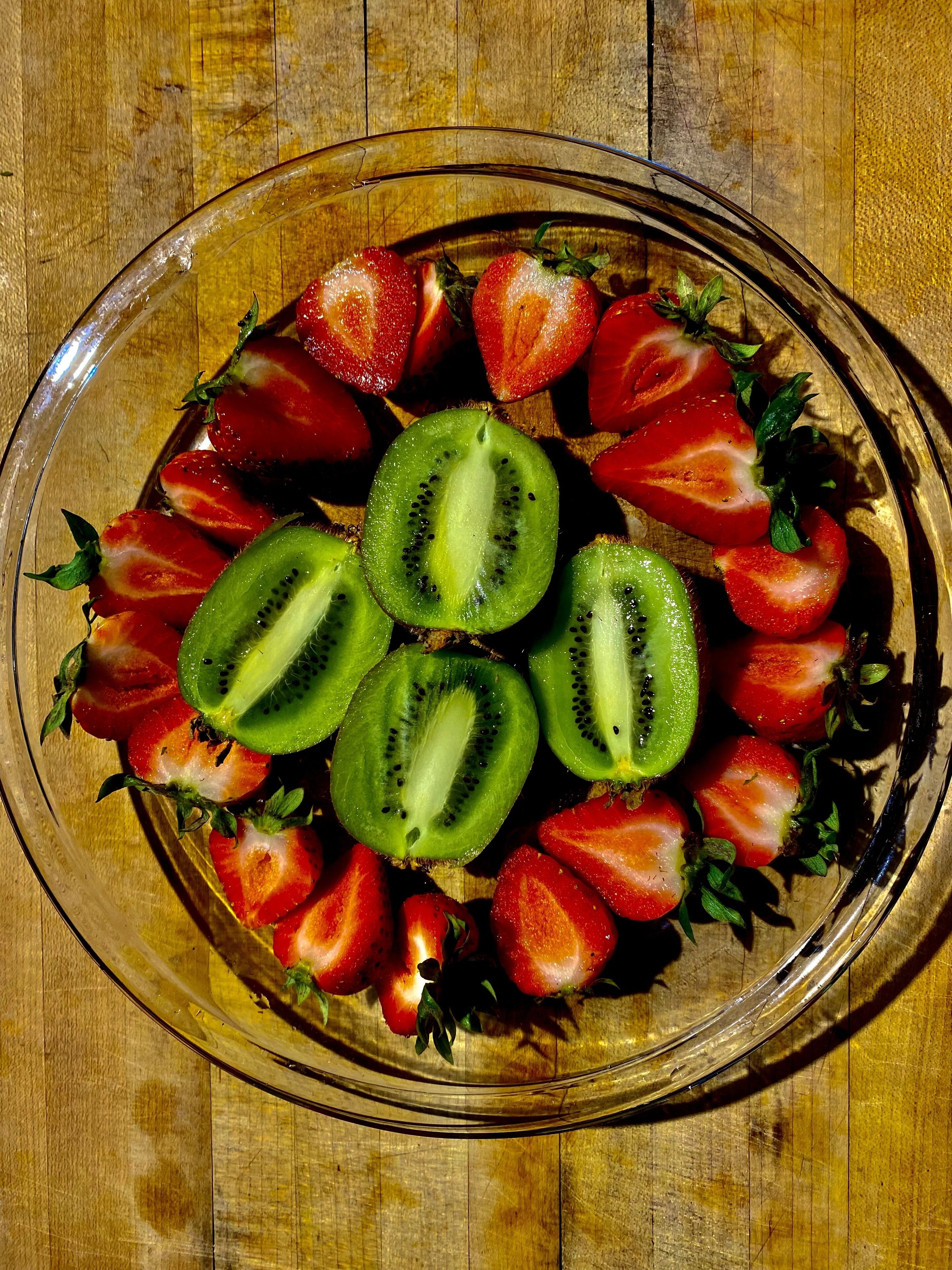 A glass bowl containing sliced strawberries and kiwi on a wooden surface.