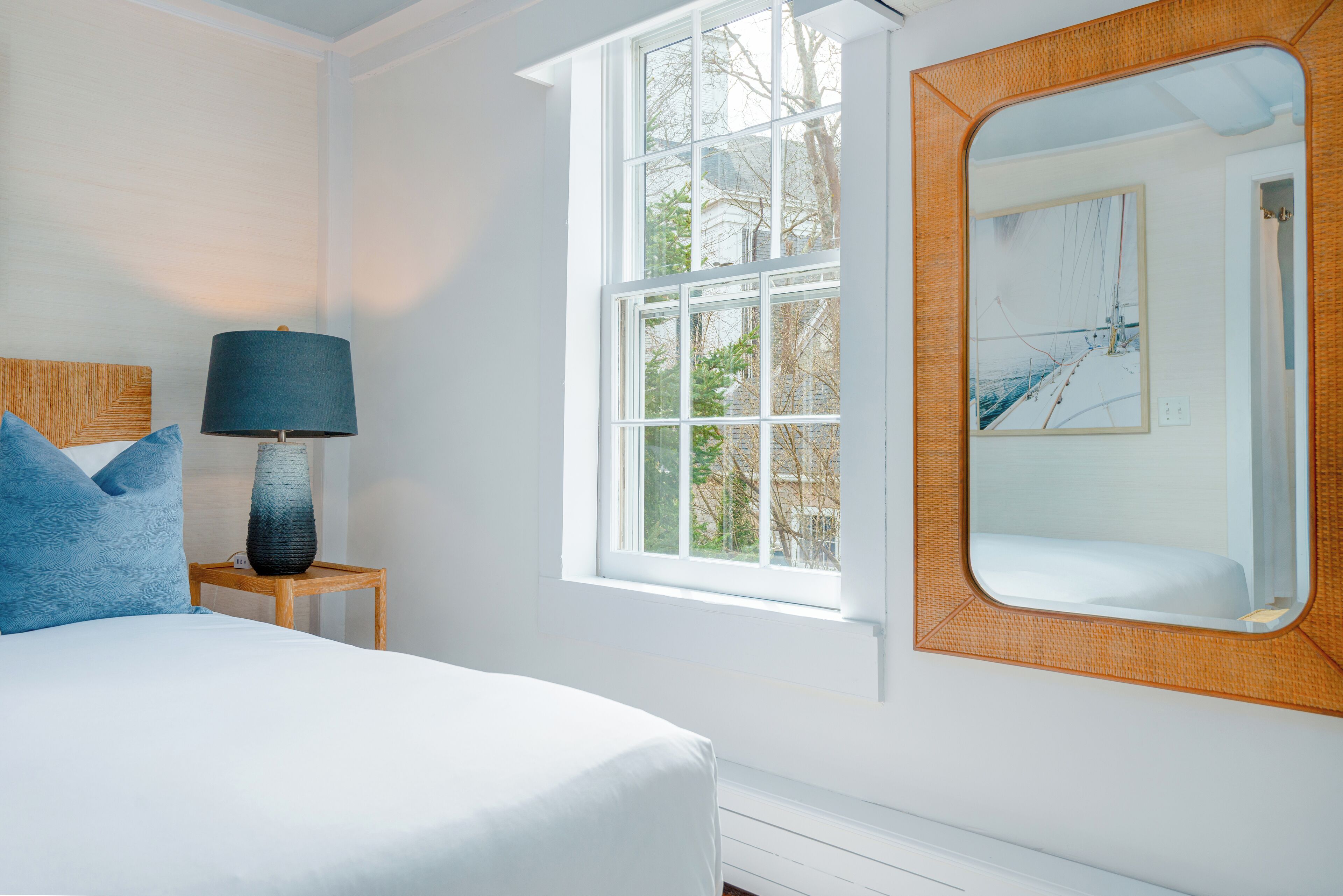 A bedroom with a bed, a nightstand, a lamp, a window, and a mirror.