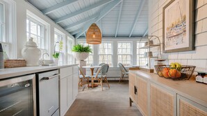 A kitchen with white cabinets, a wooden countertop, a dining area with wicker chairs, and a hanging light fixture. - Anchor Inn (Nantucket)