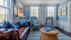 A living room with a brown leather sofa, two armchairs, a round coffee table, and a large window providing natural light. - Anchor Inn (Nantucket)