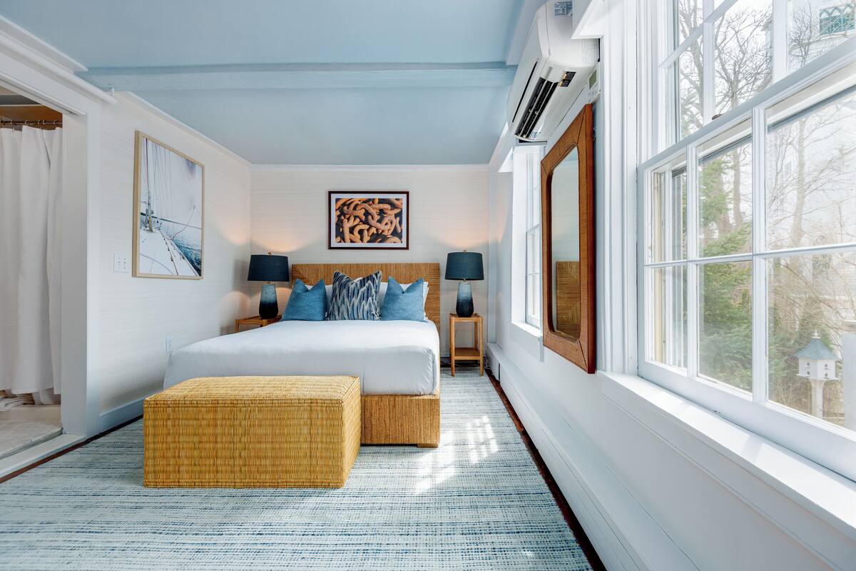 Quarto com uma cama grande, duas mesas de cabeceira, uma janela e vista para árvores.