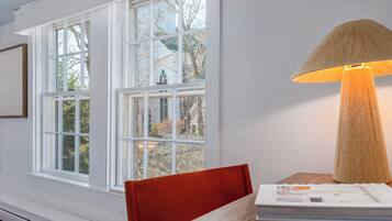 Une pièce avec de grandes fenêtres, une table avec une lampe et une chaise.