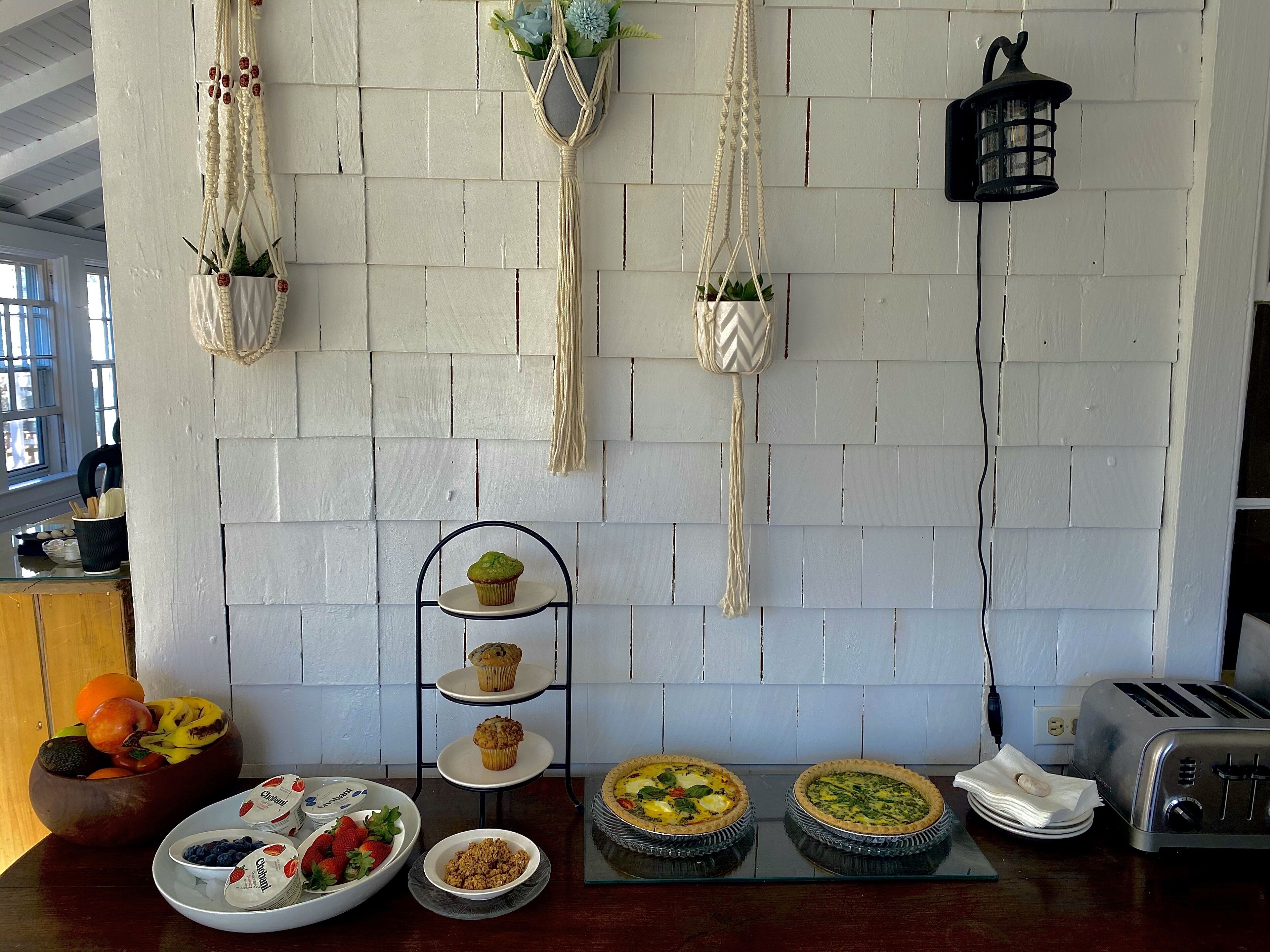 Uma bancada de cozinha com diversos alimentos, uma torradeira e vasos suspensos em macramé.
