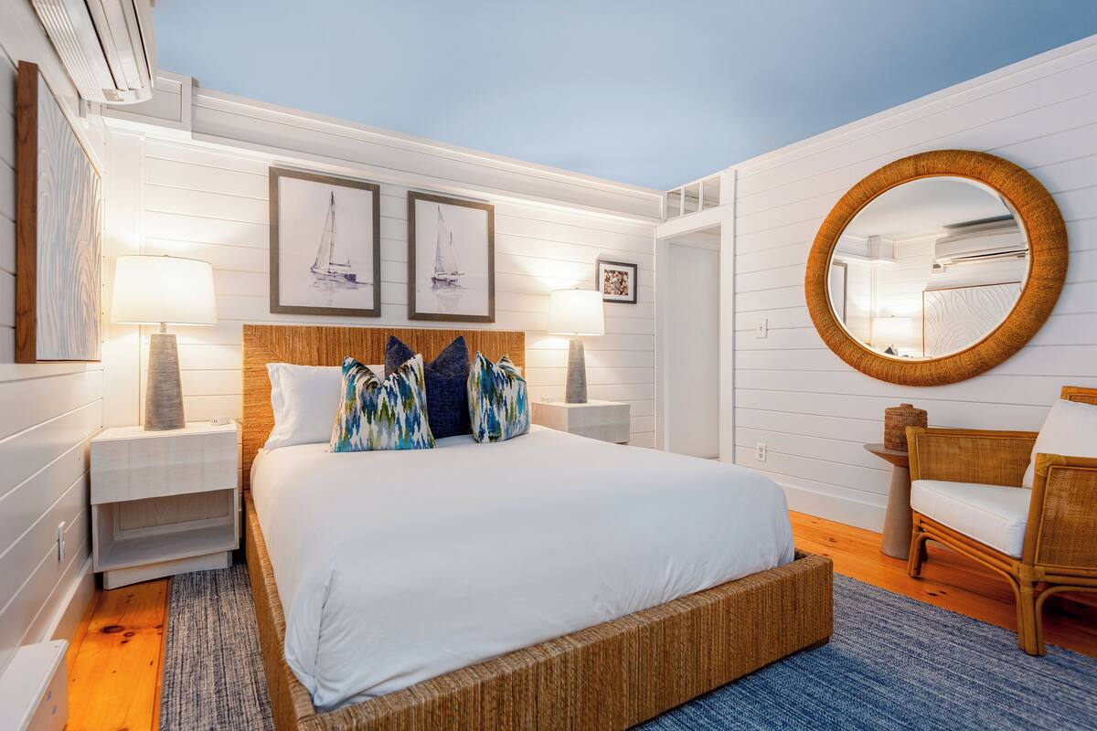 Quarto com uma cama grande, duas mesas de cabeceira, um espelho redondo e obras de arte na parede.