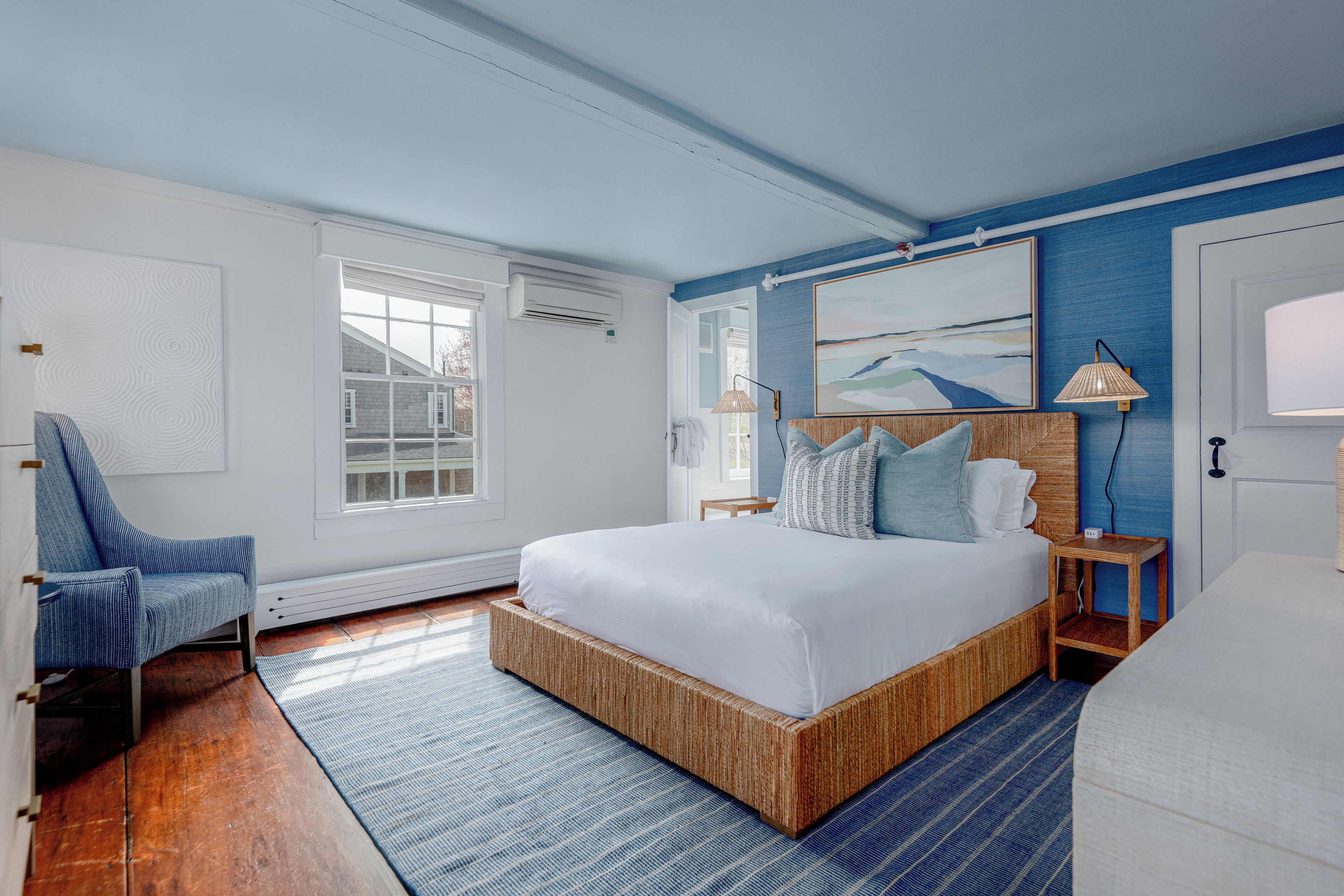 A bedroom with a large bed, a chair, a bedside table, and a painting on the wall.