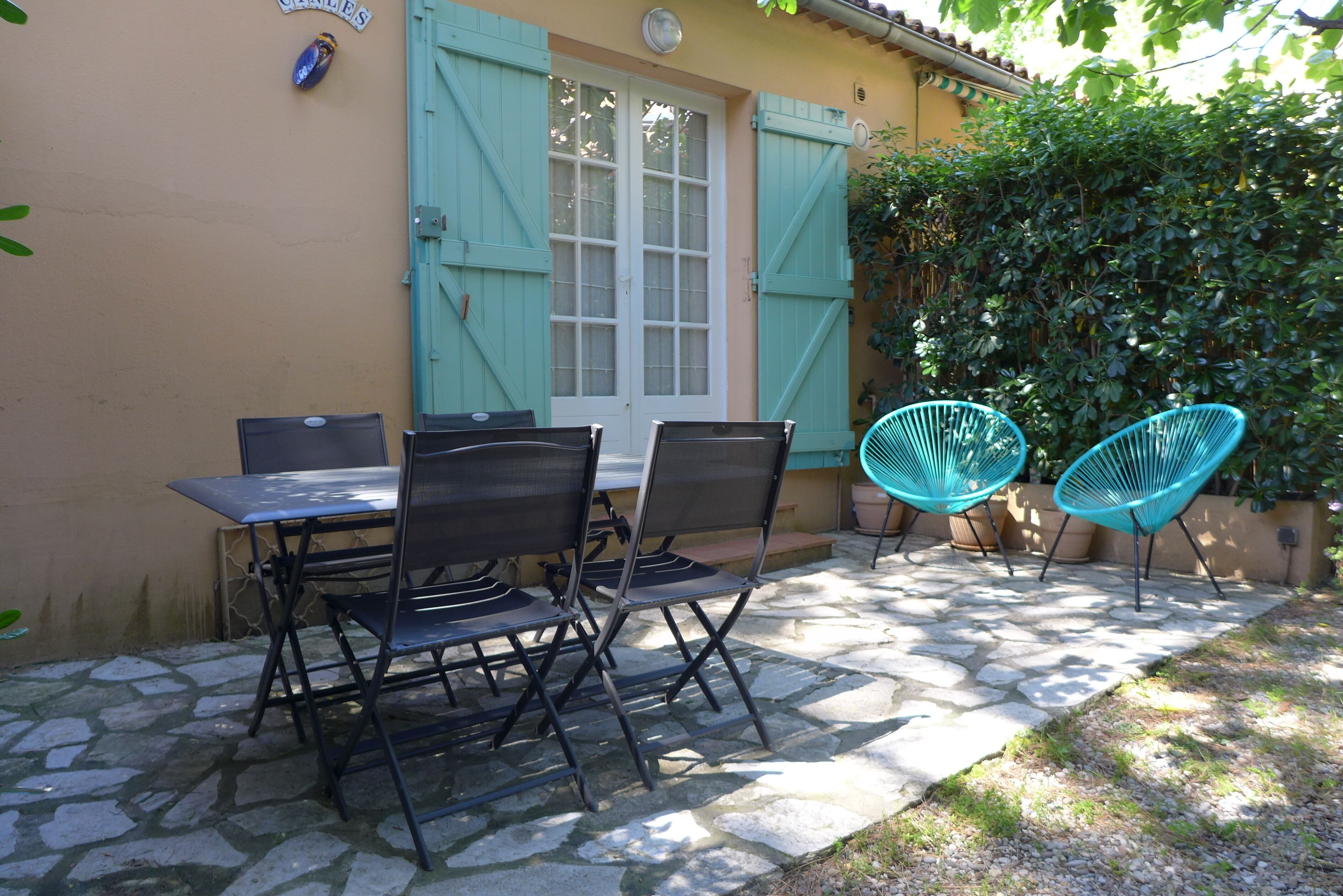 An outdoor patio with a stone floor, a table with chairs, and a window with shutters.
