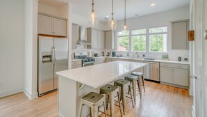 A modern kitchen with a central island, bar stools, stainless steel appliances, and pendant lighting.