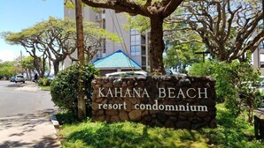 A sign for KAHANA BEACH resort condominium with a stone wall and greenery.