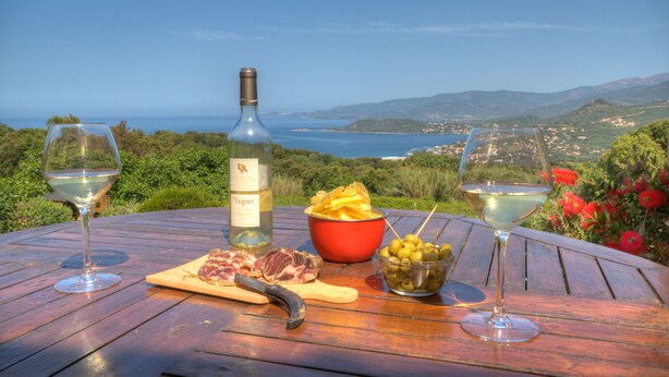 A table with a bottle of wine, two glasses, a bowl of chips, a cutting board with meat, and a bowl of olives. - Cottage 2/3 pers., Near the sea and sea view, 23 km from Ajaccio (Calcatoggio)