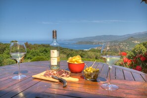 A table with a bottle of wine, two glasses, a bowl of chips, a cutting board with meat, and a bowl of olives. - Cottage 2/3 pers., Near the sea and sea view, 23 km from Ajaccio (Calcatoggio)