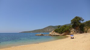 A beach with clear blue water, sandy shore, rocky outcrops, and a tree-covered hill in the background. - Cottage 2/3 pers., Near the sea and sea view, 23 km from Ajaccio (Calcatoggio)