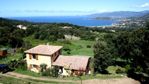 A two-story house with a tiled roof, surrounded by lush greenery and a view of the sea. - Cottage 2/3 pers., Near the sea and sea view, 23 km from Ajaccio (Calcatoggio)
