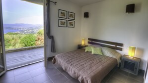 A bedroom with a large window, a bed with a headboard, two bedside tables with lamps, and four framed pictures on the wall. - Cottage 2/3 pers., Near the sea and sea view, 23 km from Ajaccio (Calcatoggio)