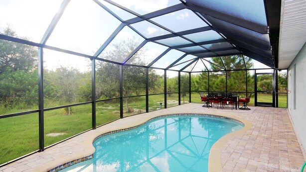 A covered swimming pool with a glass enclosure, surrounded by a patio area with outdoor furniture. - Casa del Mar (Port Charlotte)