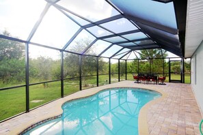 A covered swimming pool with a glass enclosure, surrounded by a patio area with outdoor furniture. - Casa del Mar (Port Charlotte)