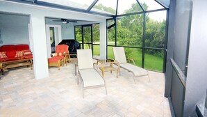 A covered outdoor area with a glass ceiling, wicker furniture, and a red sofa. - Casa del Mar (Port Charlotte)