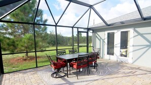 A covered patio with a table and chairs, a pool, and a view of a grassy area. - Casa del Mar (Port Charlotte)