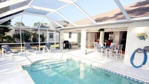A pool area with a clear pool, white lounge chairs, and a covered patio. - Lauras Paradise (Rotonda West)