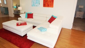 A modern living room with a white sectional sofa, red and blue patterned throw pillows, a red tray with glasses, and two abstract paintings on the wall. - Lauras Paradise (Rotonda West)