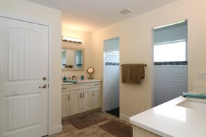 A bathroom with a white door, a vanity with a mirror, a towel rack, and a window with a view of the outside. - Blue Marlin (Port Charlotte)