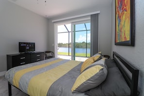 Ein Schlafzimmer mit Bett, Fernseher, Sessel und Seeblick durch große Fenster.